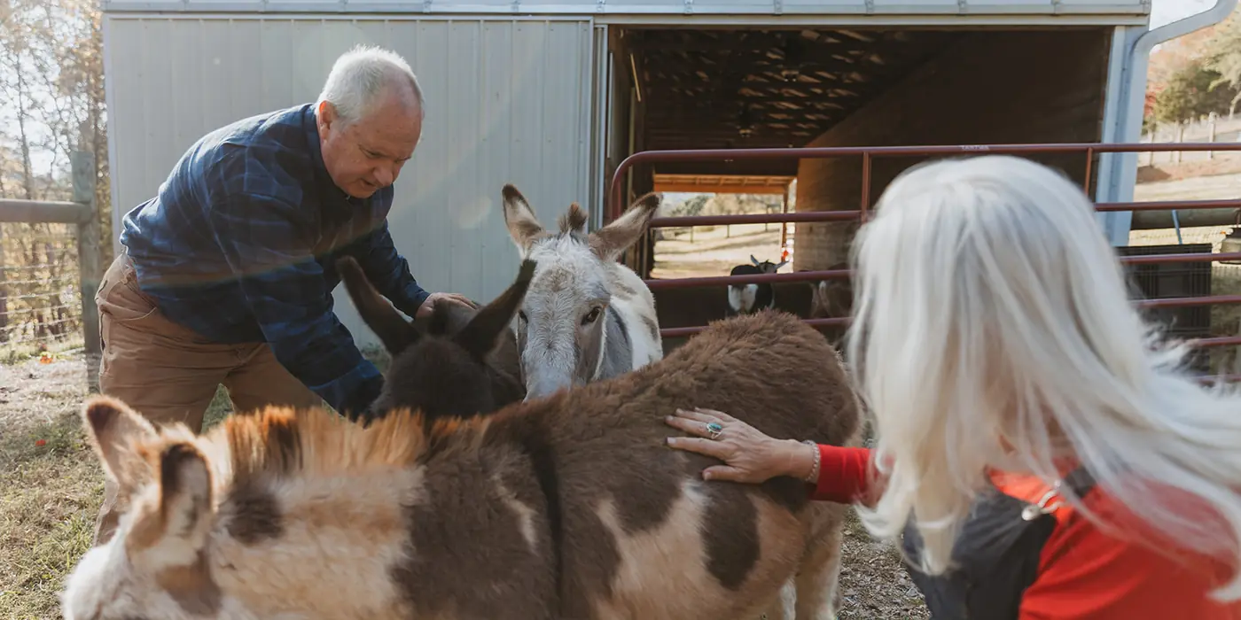 Lane and Jules Morris kneeling with four mini donkeys outside the barn, beside a red pipe gate