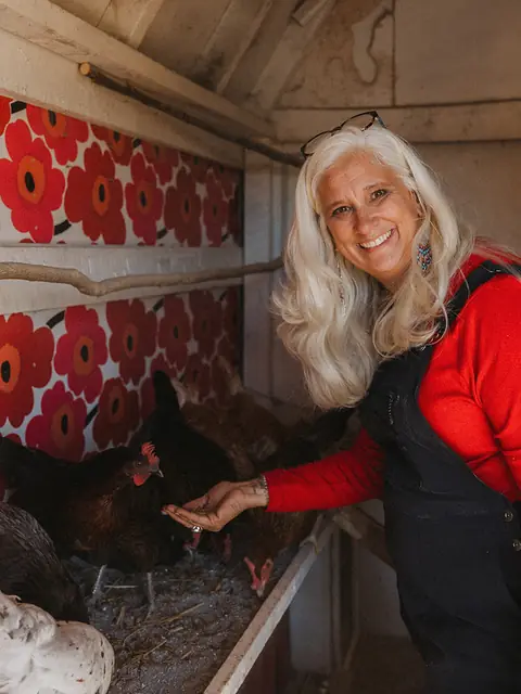 Jules smiling as she hand-feeds the hens along the roost in the flower-papered coop