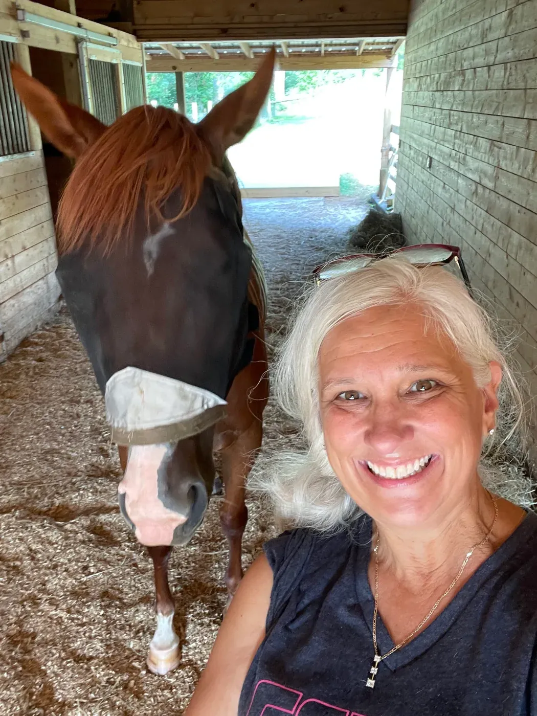 Jules Morris smiling in the barn aisle beside a chestnut rescue horse with a blaze face